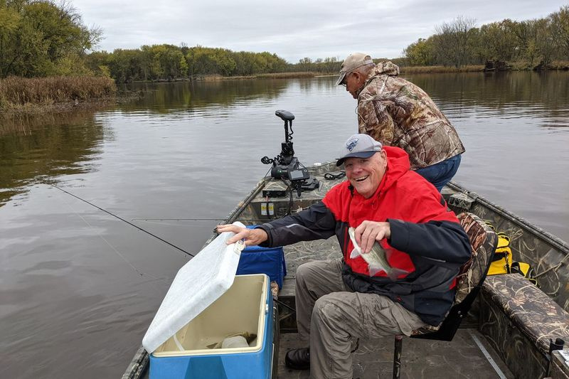 Bruce Zolna lancia uno dei primi bassi bianchi nel frigorifero mentre la guida Bill Stoeger lavora a prua della barca sul fiume Wolf. Attestazione: Dale Bowman