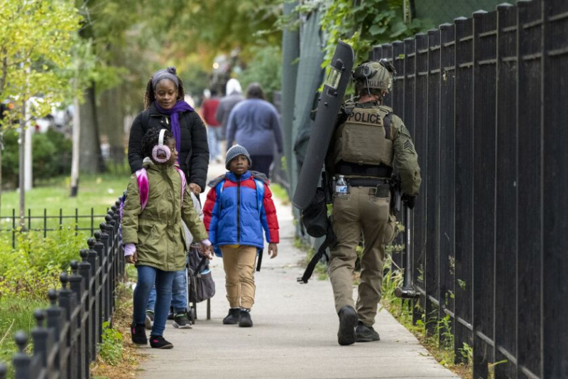   Een SWAT-officier van de Chicago Police Department, met een schild, een voorhamer en een geweer, loopt langs een gezin terwijl agenten reageren op meldingen van een mogelijke gewapende man die is gebarricadeerd in een appartementencomplex in het 6000-blok van North Winthrop Avenue in Edgewater aan de noordkant, dinsdag , 18 oktober. Een persoon werd in hechtenis genomen na een 14 uur durende impasse met het SWAT-team.