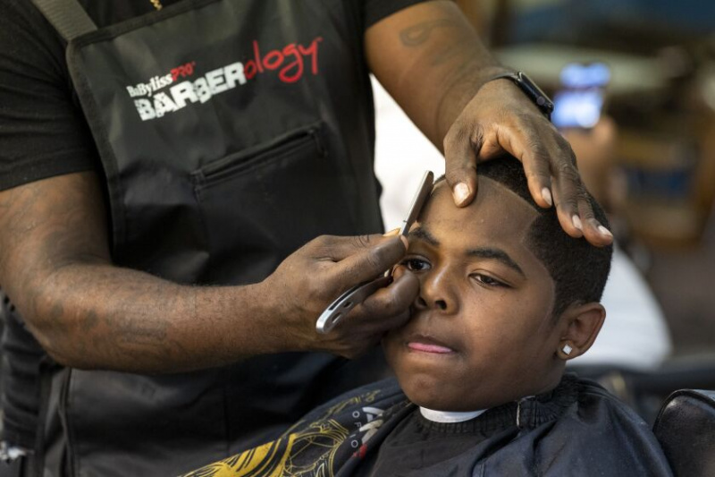   Barber Mario Tate memotong rambut Devin Alexander yang berusia 10 tahun di Urban Professional Grooming, yang menyertai 23 September dengan Brilliant Brown Boys Book Club untuk acara “Fades, Fros & Perkongsian buku', di Chatham di South Side. Kanak-kanak lelaki yang datang untuk menggunting rambut boleh memilih dari rak buku yang lengkap jika mereka mahukan sesuatu untuk dibaca sementara mereka menunggu.