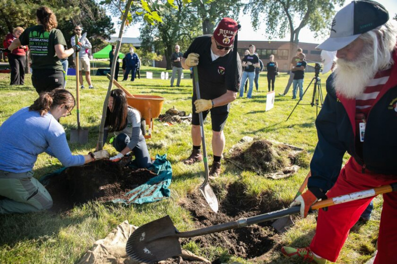   Sukarelawan menunjukkan cara menanam pokok semasa upacara penanaman pokok untuk meraikan ulang tahun ke-100 hospital Shriners Children's Chicago di luar hospital, Selasa, 4 Okt. Sukarelawan yang bekerja di hospital dan dalam syarikat rakan kongsi seperti One Tree Planted, DocuSign, Mars Candy dan Institut Perkhidmatan Muzium dan Perpustakaan menanam 15 pokok di bawah bimbingan kakitangan Inisiatif Pokok Wilayah Chicago.