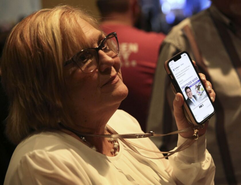   Robin Best uit Vandalia, Illinois, houdt haar telefoon omhoog en toont een rapport van Fox 2 News dat Democraat J.B. Pritzker werd herkozen als gouverneur van Illinois op een Darren Bailey-wachtfeest op dinsdag 8 november.