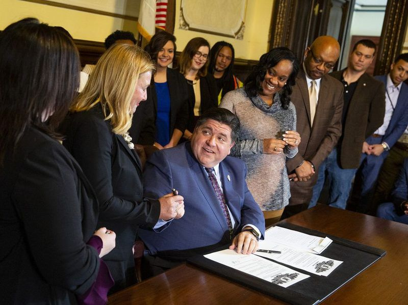 Guvernér štátu Illinois JB Pritzker ponúka pero štátnej zástupkyni Anne Moellerovej, D-Elgin, ktorá spolu so senátorkou Cristinou Castro, D-Elginovou odišla, sponzoruje návrh zákona, ktorý zakazuje zamestnávateľom pýtať sa na platovú históriu na pohovoroch počas tlačová konferencia a