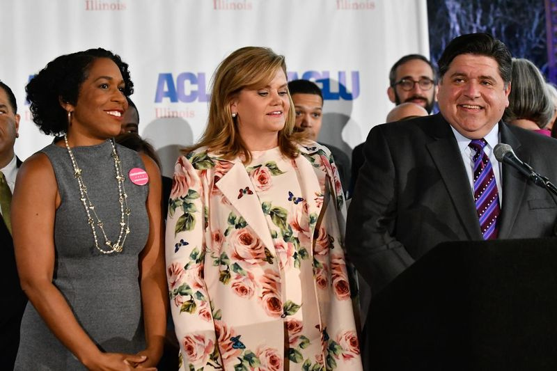 Illinois first lady M.K. Pritzker, tweede van links, kijkt toe terwijl gouverneur J.B. Pritzker spreekt tijdens een persconferentie in 2019. Luitenant-gouverneur Juliana Stratton, links, was ook aanwezig.