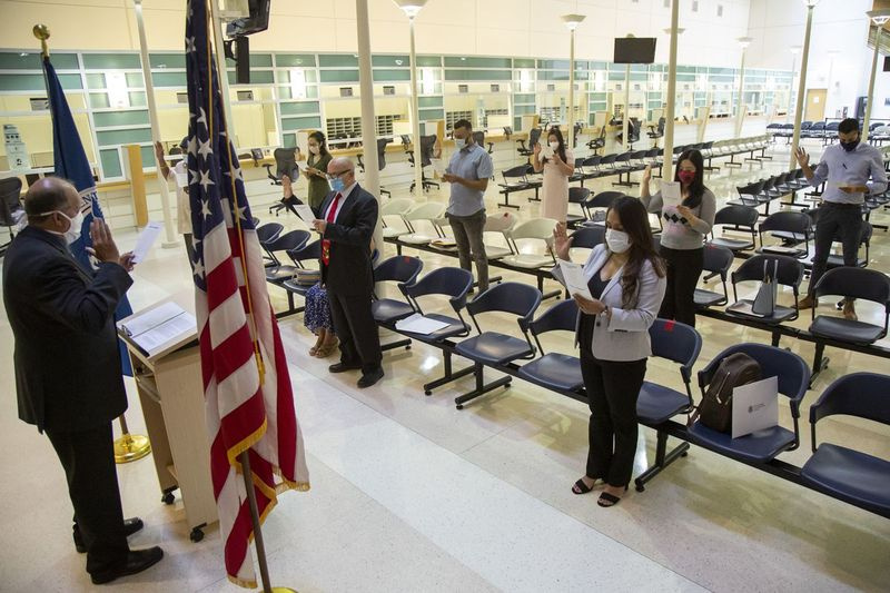 Lidé zvednou ruku pro přísahu věrnosti během společensky vzdáleného naturalizačního obřadu v kanceláři US Citizenship and Immigration Services na 101 W. Ida B. Wells Drive v South Loop.