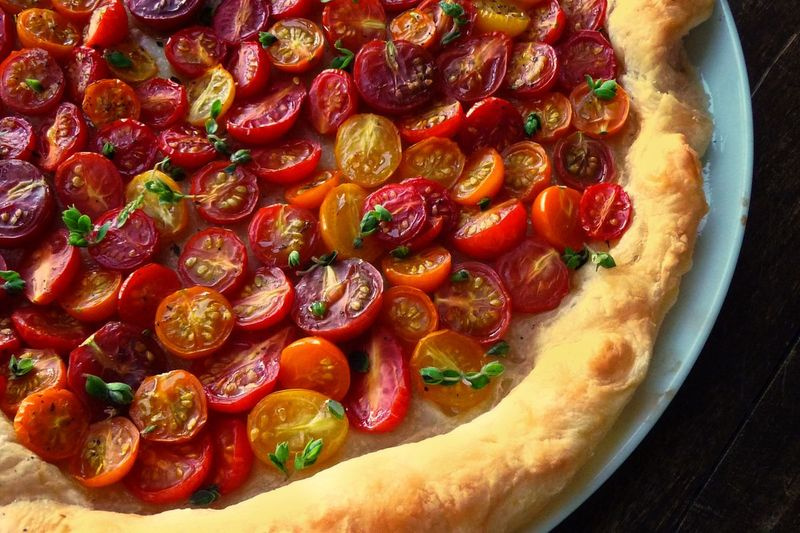 Les tomates sucrées et juteuses occupent une place centrale dans cette tarte, car elles sont nichées sur un lit de pâte feuilletée aérée saupoudrée de fromage aux noix et d