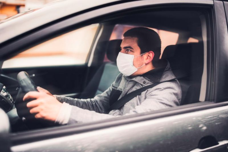 Man met een masker zit in een auto met zijn handen aan het stuur. Uber-chauffeurs kunnen een vaccinatieafspraak boeken via het planningssysteem van Walgreens met behulp van een code die via de Uber-app wordt verzonden.