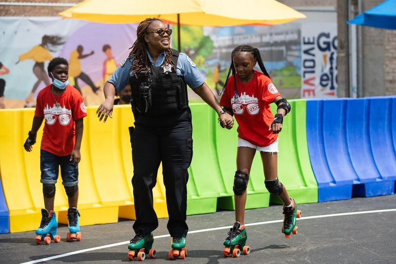 En polis åker skridskor med ett barn på Garfield Park Community Plaza och Outdoor Roller Rink under öppningsdagen i området West Garfield Park, fredag ​​eftermiddag den 23 juli 2021.